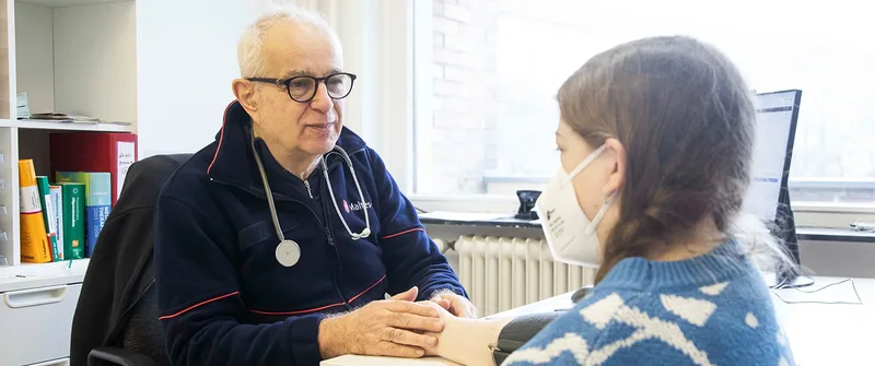 Malteser-Arzt misst in einem Behandlungszimmer den Blutdruck einer Patientin mit einer Oberarmmanschette