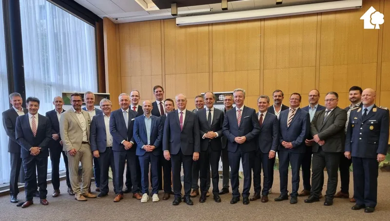 Bundeswehr: Eine Gruppe von Vertretern der Bundeswehr und Partnerunternehmen posiert für ein gemeinsames Foto anlässlich einer Projektvergabe. Im Hintergrund ist ein Informationsbanner mit dem Logo der Bundeswehr zu sehen, während auf der rechten Seite ein Soldat im Dienstanzug der Bundeswehr steht.
