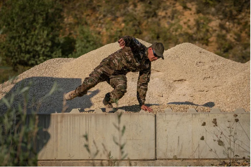 Soldat in Gore-Einsatzbekleidung überwindet während einer Ausbildung auf einem Übungsgelände eine Betonbarriere