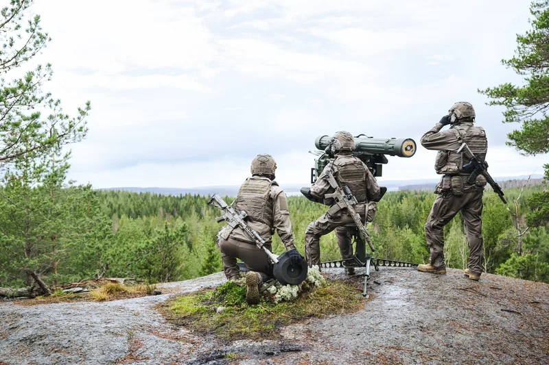 Drei Soldaten in moderner Ausrüstung bedienen auf einer felsigen Anhöhe das schwedische Flugabwehrsystem RBS 70 NG von Saab.