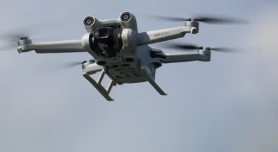 Drohne DJI Mini 3 Pro im Flug vor bewölktem Himmel mit sichtbarer Frontkamera und Hinderniserkennungssensoren