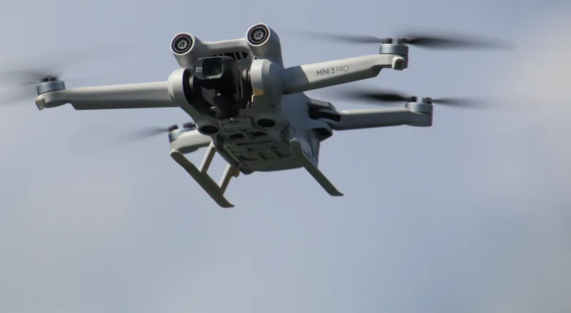 Russland: Drohne DJI Mini 3 Pro im Flug vor bewölktem Himmel mit sichtbarer Frontkamera und Hinderniserkennungssensoren