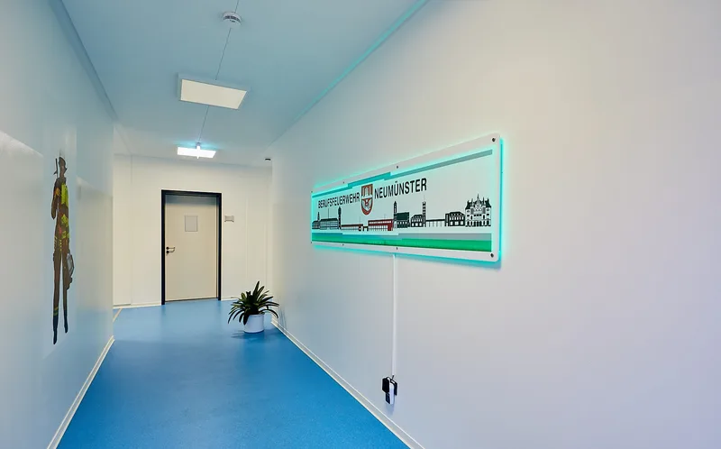 Flur einer modularen Rettungswache von Adapteo der Berufsfeuerwehr Neumünster mit beleuchtetem Logo und Wandgrafik einer Einsatzkraft