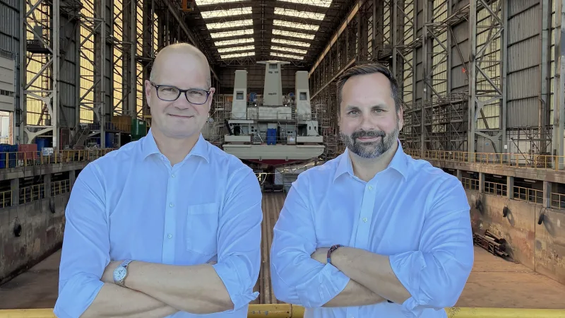 Frank Mallon von der Flensburger Schiffbau-Gesellschaft und Max Berger von STARK in einer Werfthalle vor einem im Bau befindlichen Schiff