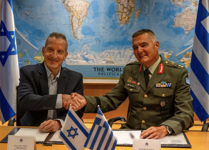 Generalmajor Amir Baram und Generalmajor Bouras schütteln sich bei einer Unterzeichnung vor israelischen und griechischen Flaggen die Hand