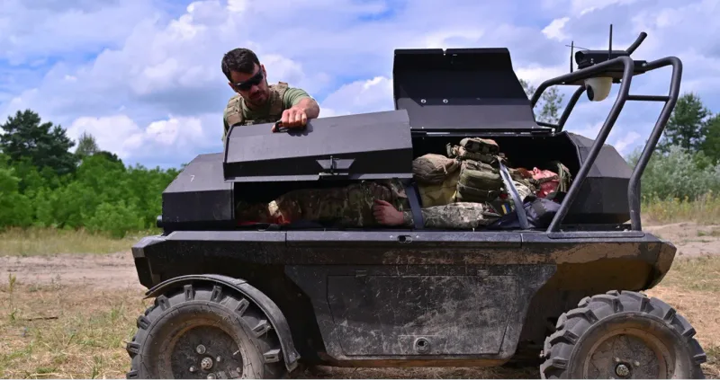 A soldier demonstrates the recovery of a casualty using the unmanned ground vehicle MAUL. The injured soldier lies in a protected transport bay of the four-wheeled, all-terrain UGV.