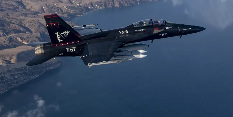 Boeing F/A-18F Super Hornet der US Navy in schwarzer Sonderlackierung der VX-9 mit Luft-Luft-Lenkwaffen im Flug über dem Meer