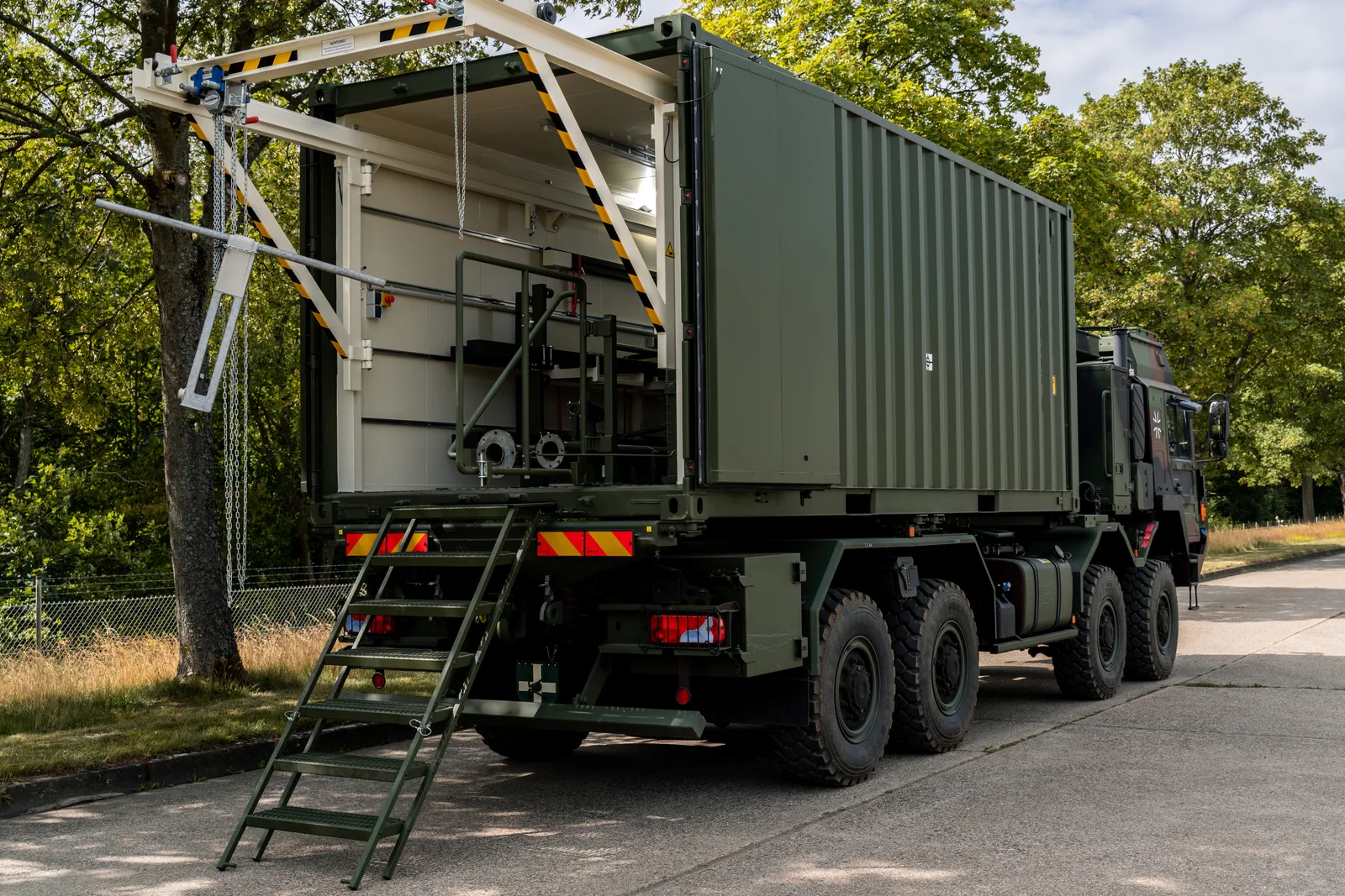 MAN-Lkw der Bundeswehr mit geöffnetem Rüstsatzträger-Container, ausklappbarer Treppe und Hebevorrichtung am Heck auf einer Straße