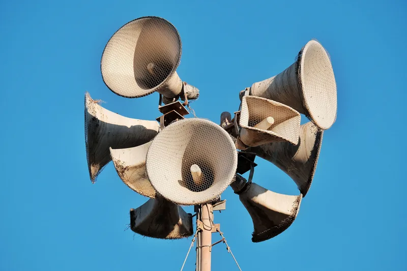 Warntag: Auf einem Mast montierte Trichterlautsprecher einer Sirenenanlage vor blauem Himmel