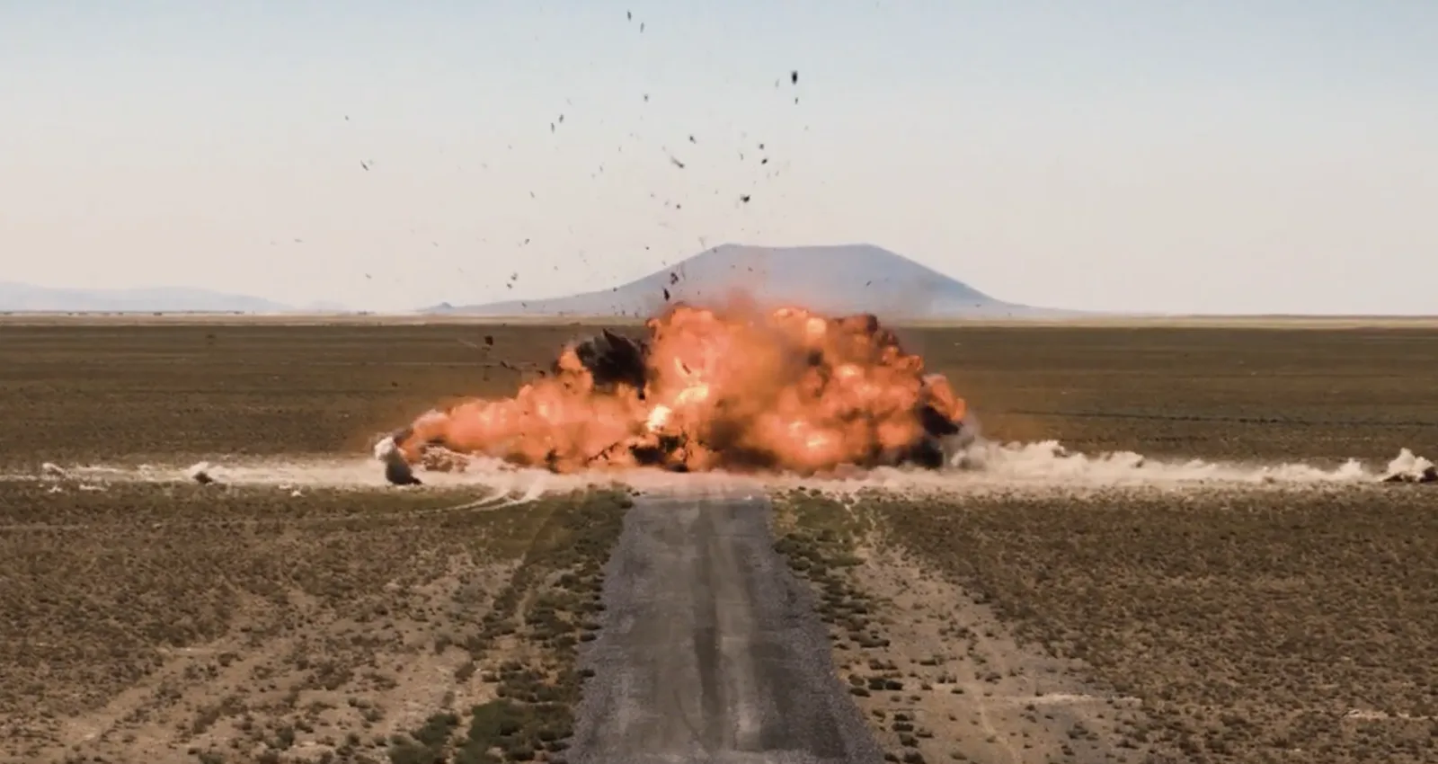 Heftige Detonation mit Feuer- und Staubwolke auf einem unbefestigten Weg in einer kargen Steppenlandschaft