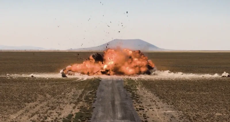 Heftige Detonation mit Feuer- und Staubwolke auf einem unbefestigten Weg in einer kargen Steppenlandschaft