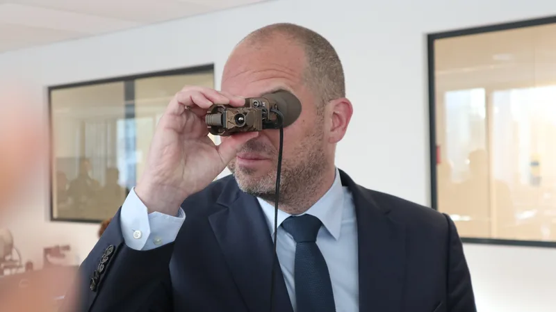 Mann im Anzug blickt in einem Präsentationsraum durch ein kompaktes, handgehaltenes Wärmebildgerät