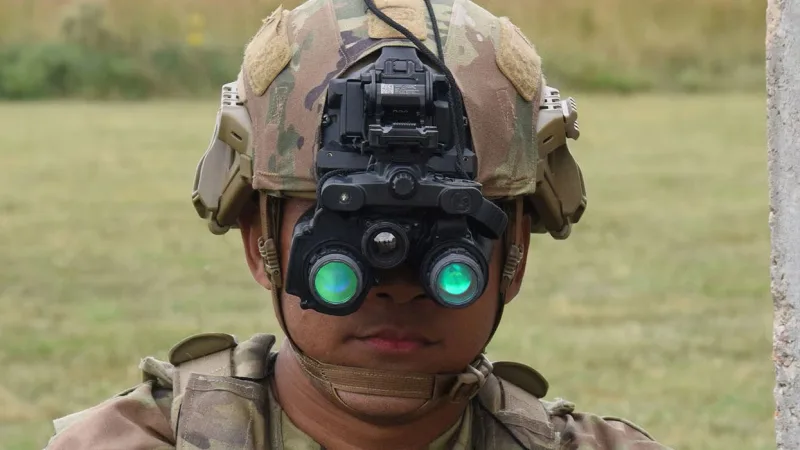 US-Soldat mit am Helm montierter ENVG-B Nachtsichtbrille und optischer Visierung auf einer Handwaffe im Vordergrund