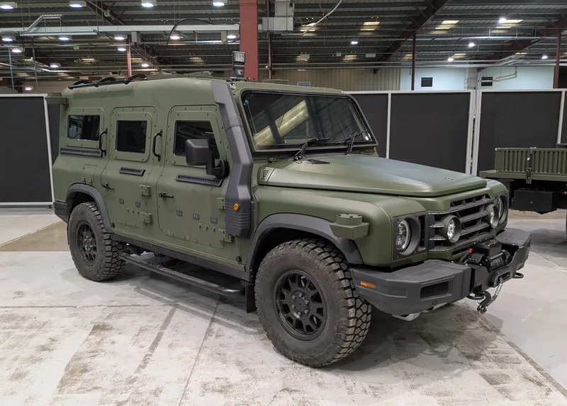 Olivgrünes geschütztes Geländefahrzeug Ineos Grenadier EPV mit Panzerung und Frontseilwinde in einer Ausstellungshalle