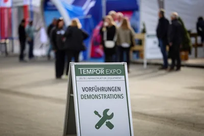 Hinweisschild für Vorführungen auf der Fachmesse Tempor Expo vor unscharfen Besuchern auf dem Ausstellungsgelände
