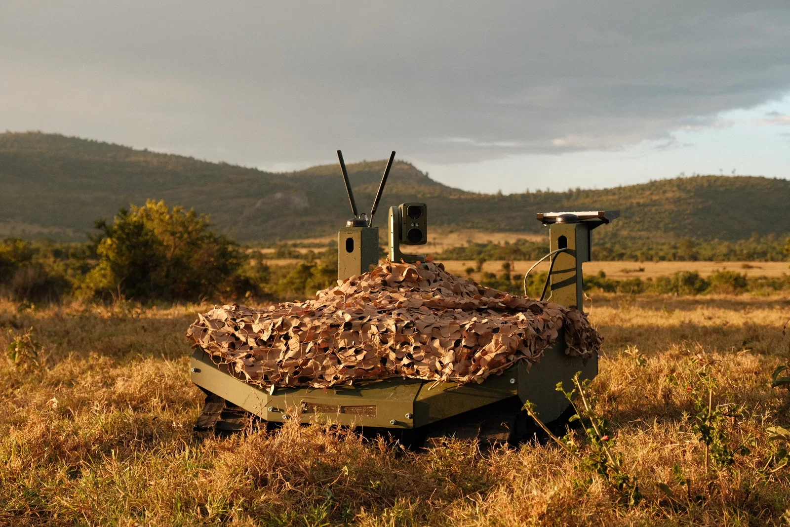 Unbemanntes Bodensystem GEREON von ARX Robotics mit Tarnnetz, Optronik und Antennen in einer Graslandschaft