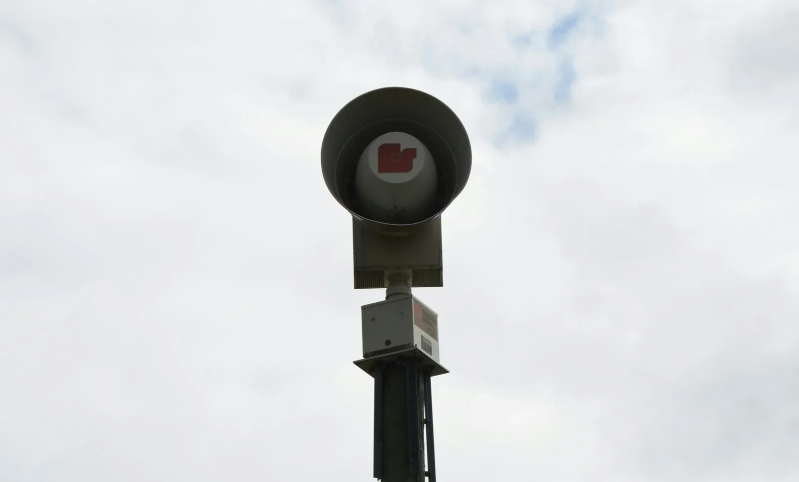 Warntag: Elektronische Sirene des Herstellers Hörmann auf einem Holzmast vor bewölktem Himmel