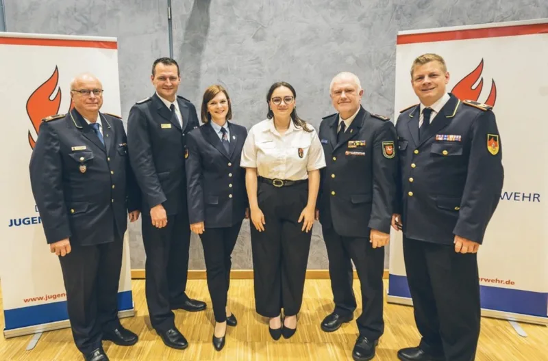 Sechs Angehörige der Deutschen Jugendfeuerwehr in Dienstuniformen posieren vor zwei Roll-up-Bannern der Organisation