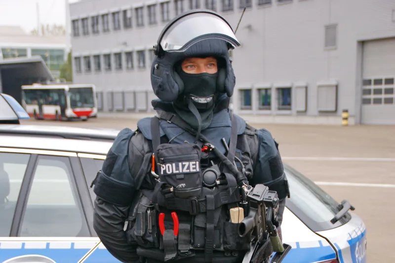 Thüringen: Einsatzkraft einer polizeilichen Spezialeinheit in schwerer Schutzausrüstung mit Heckler & Koch Maschinenpistole vor einem BMW-Streifenwagen