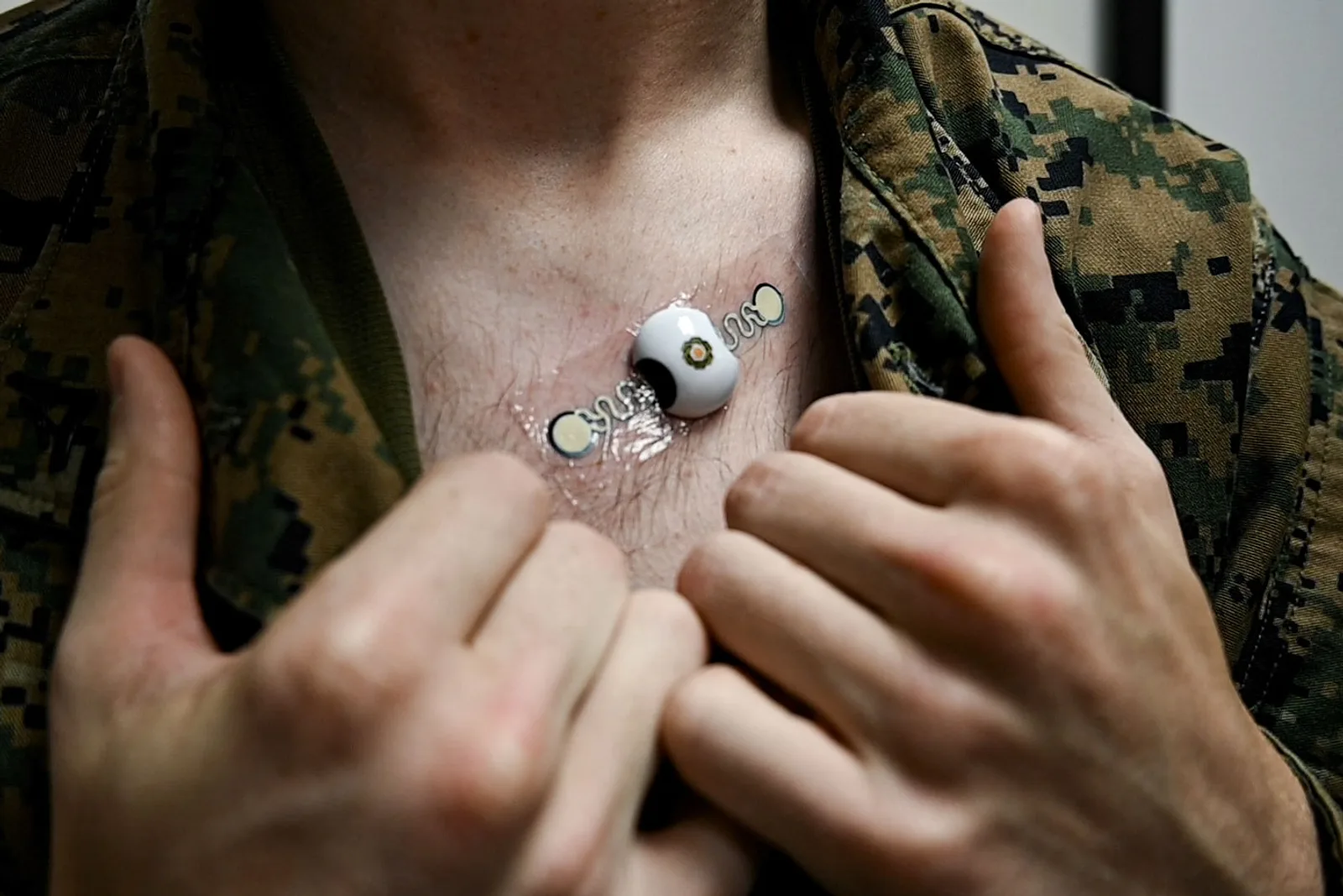 Soldat in Tarnuniform mit einem auf der Brust befestigten medizinischen Sensor zur Erfassung von Vitaldaten mittels Pflaster