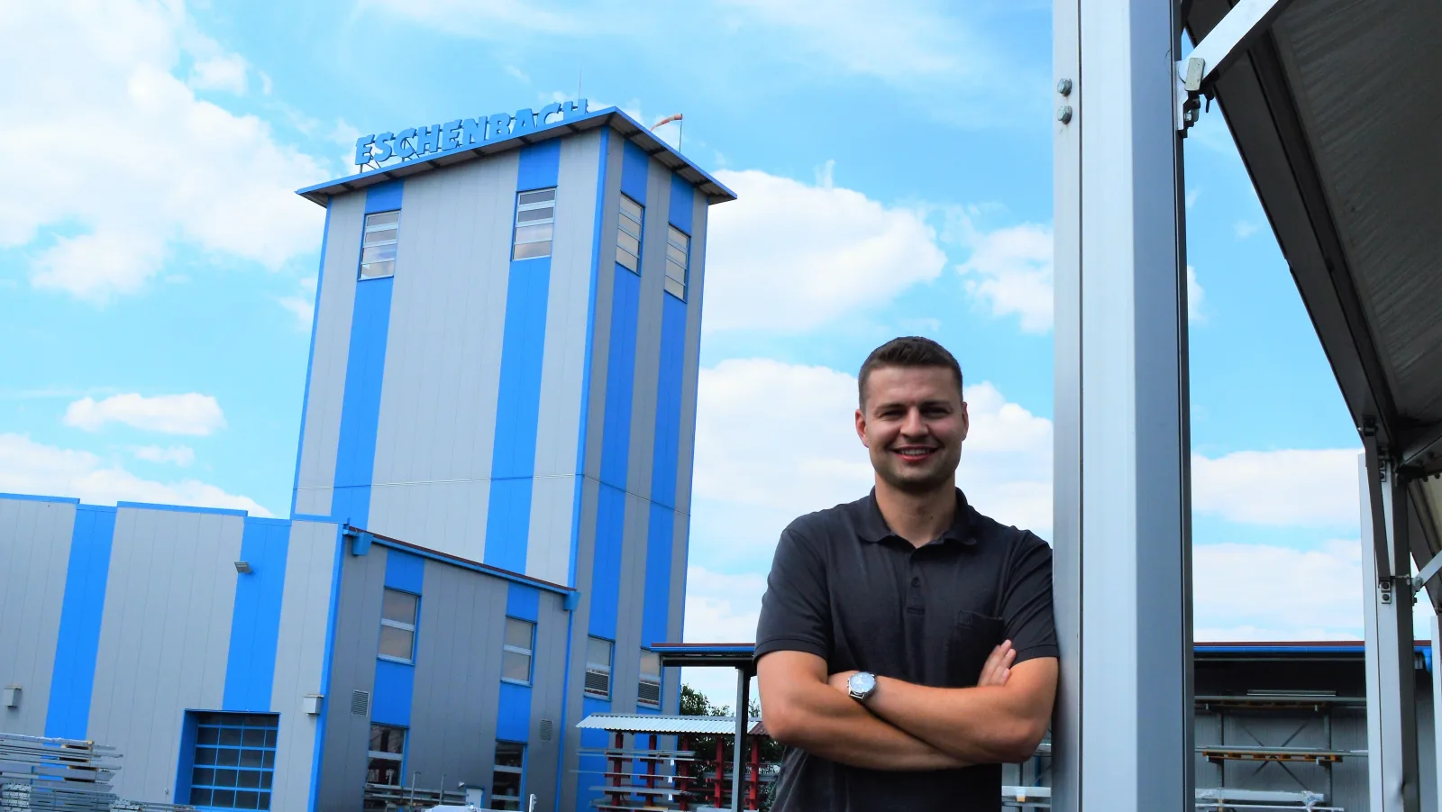 Dezentrale Logistik: Philipp Eschenbach steht vor dem Firmengebäude der Firma Eschenbach mit dem markanten Turm und blauem Schriftzug im Hintergrund