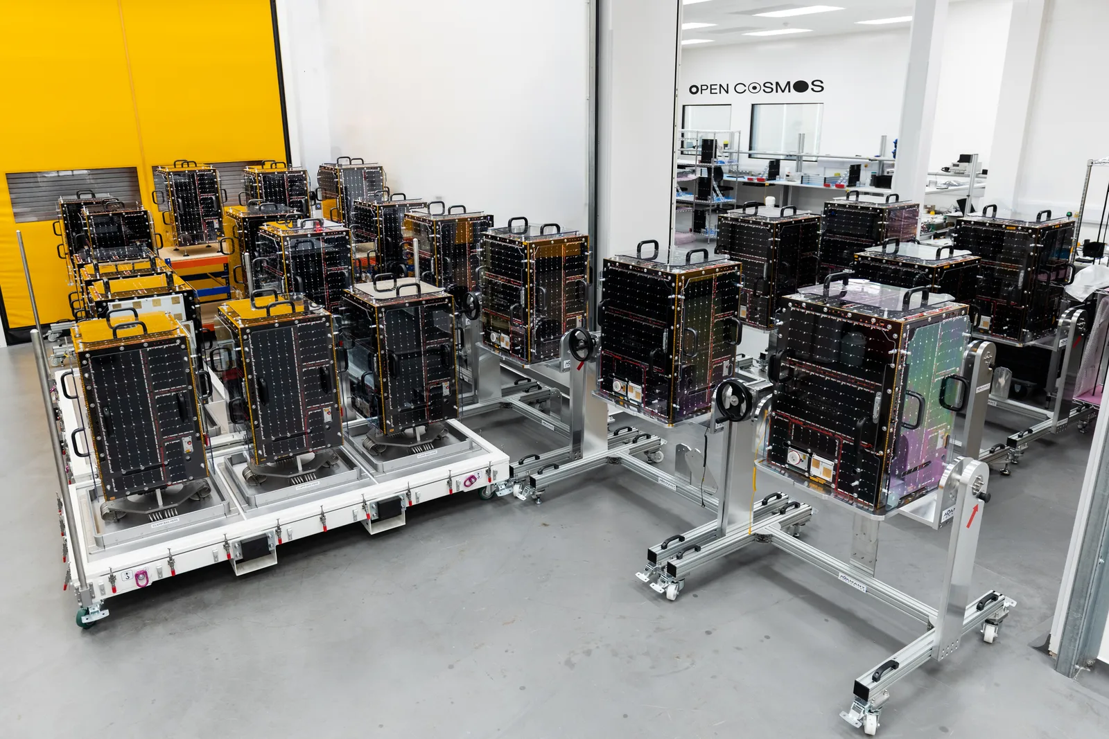 Mehrere Kleinsatelliten auf Montagevorrichtungen in einer Reinraum-Fertigungshalle von Open Cosmos