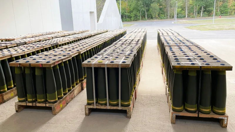 Großkalibrige Artilleriegranaten in Holzgestellen auf Transportpaletten vor einem modernen Munitionsdepot