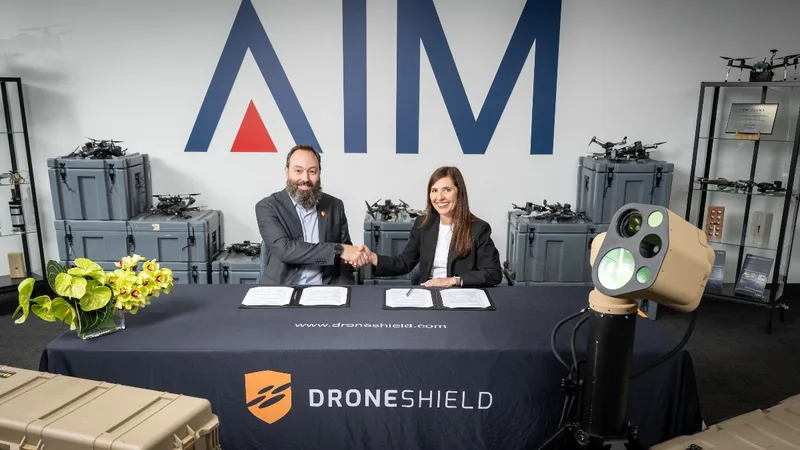 Vertreter von DroneShield und AIM Defence besiegeln eine Kooperation vor einem optischen Drohnenabwehrsystem und Drohnentechnik