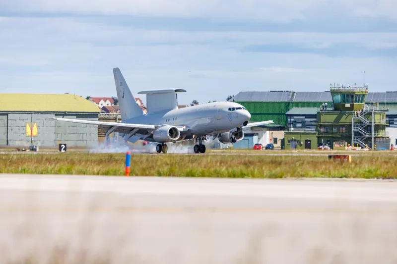 Boeing E-7A Wedgetail der Royal Air Force landet mit rauchenden Reifen auf einem Flugplatz vor Hangars und einem Kontrollturm