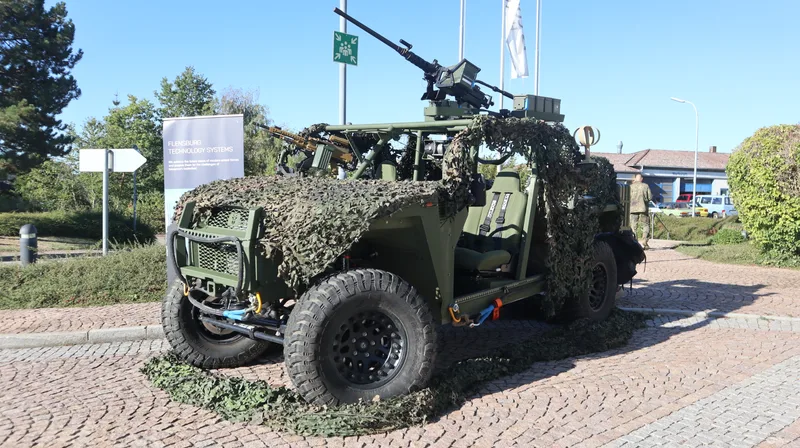 Mit Tarnnetzen ausgestattetes Geländefahrzeug von Flensburg Technology Systems mit Maschinengewehren auf Drehring- und Beifahrerlafette