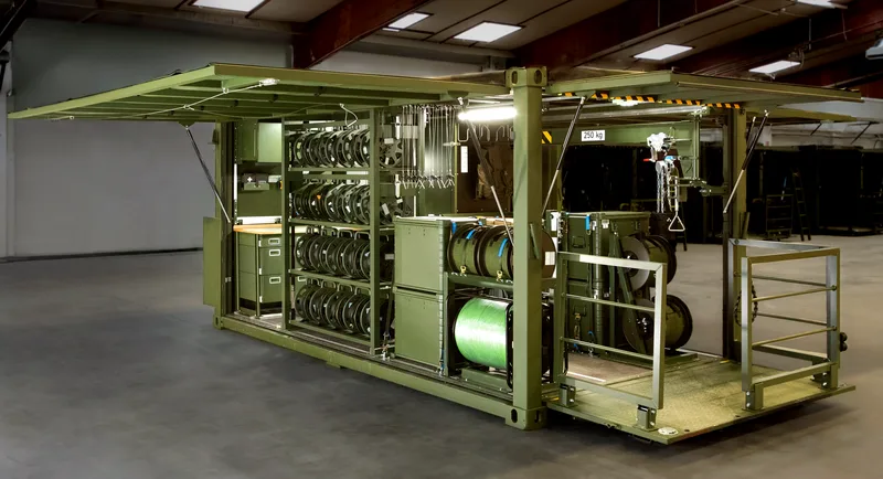 Geöffneter olivgrüner Militärcontainer als mobile Werkstatt mit Regalen, Kabeltrommeln, Werkstattschränken und integriertem Schwenkkran