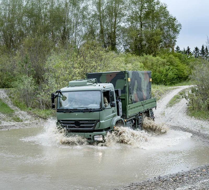 Militärischer LKW Mercedes-Benz Axor der Bundeswehr mit zwei Soldaten in Flecktarn durchquert eine Furt auf einem Übungsgelände