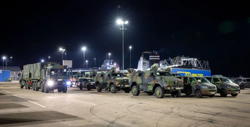 Bundeswehr-Fahrzeuge vom Typ ATF Dingo 2, VW-Transporter und MAN-Lkw stehen nachts zur Verschiffung an einem Hafen vor einer Fähre