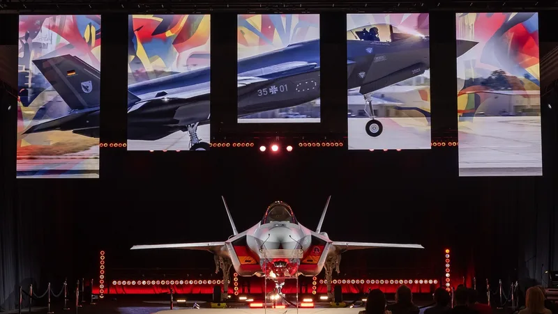 Lockheed Martin F-35 Lightning II der Bundeswehr mit Kennung 35+01 auf einer Präsentationsbühne vor Bildschirmen