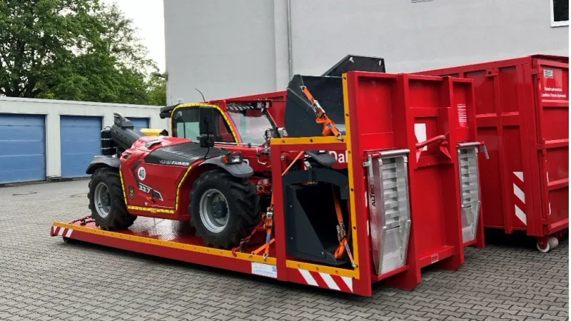 Teleskoplader Merlo Turbofarmer 33.7 verzurrt auf einer roten Abrollplattform vor einem Katastrophenschutz-Container und Gebäude