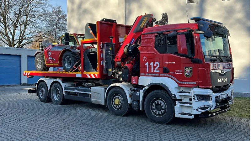 Wechselladerfahrzeug MAN TGS der Feuerwehr Dahme-Spreewald mit Palfinger-Kran transportiert einen Merlo-Teleskoplader auf einem Hof