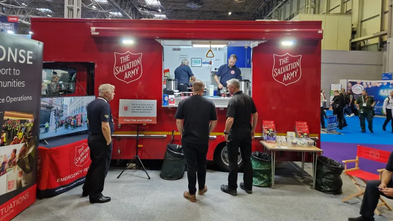 Rotes Verpflegungsfahrzeug der Salvation Army auf einer Fachmesse für Rettungskräfte mit Mitarbeitern und Besuchern am Messestand
