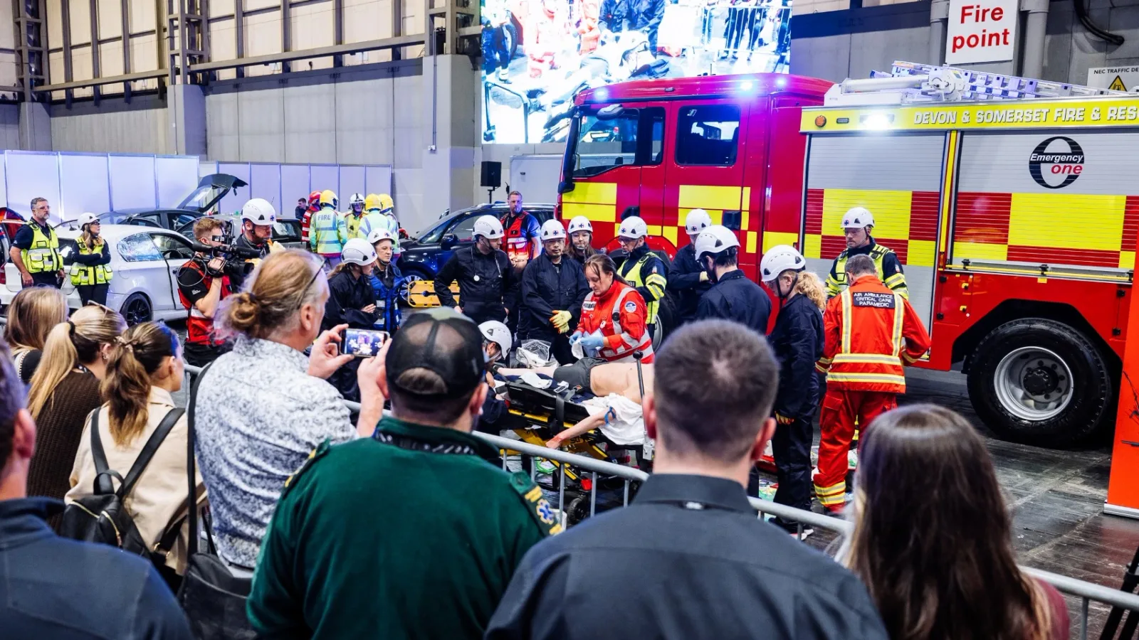 Einsatzkräfte demonstrieren medizinische Erstversorgung vor einem Emergency One Löschfahrzeug der Devon & Somerset Feuerwehr auf einer Fachmesse
