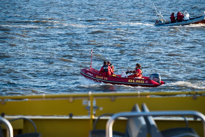 DLRG-Rettungsboot von Zodiac mit Yamaha-Außenbordmotor und drei Einsatzkräften auf dem Wasser vor einem Boot der Wasserschutzpolizei