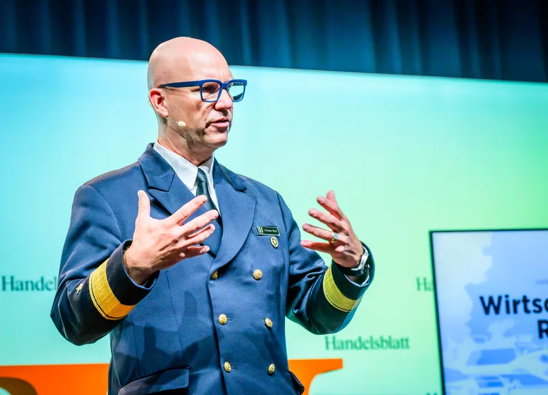 Flottillenadmiral Christian Bock in Dienstuniform der Deutschen Marine spricht gestikulierend vor einer Handelsblatt-Rückwand