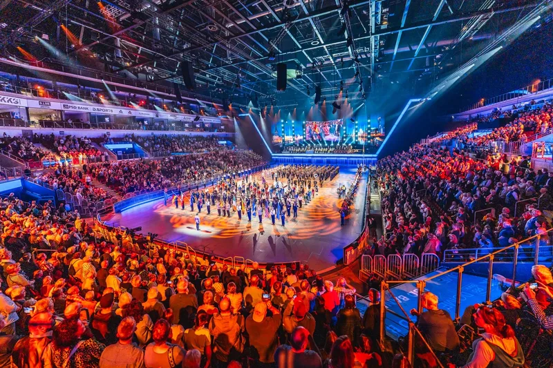 Internationale Militärorchester und Fahnenträger treten vor Publikum im beleuchteten PSD Bank Dome in Düsseldorf auf