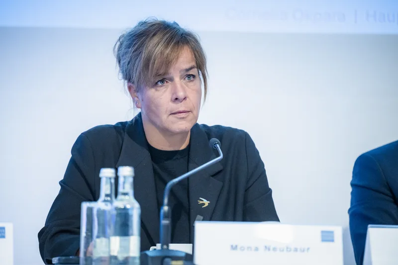 Mona Neubaur bei einer Podiumsdiskussion mit Mikrofon und Namensschild auf einem Tisch vor ihr