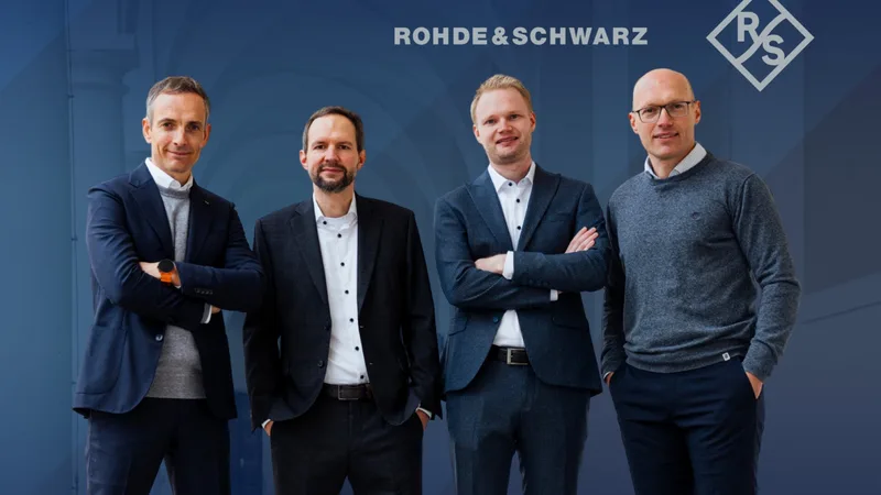 Vier Männer in Anzügen posieren vor einem blauen Hintergrund mit dem Logo des Technologiekonzerns Rohde & Schwarz
