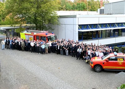 BKS: Gruppenfoto von Einsatzkräften der LFbK Rheinland-Pfalz vor einem Löschfahrzeug und einem roten Ford Ranger Einsatzfahrzeug