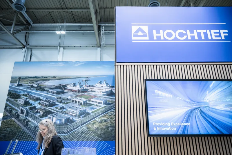 Messestand von Hochtief auf einer Fachmesse mit digitaler Projektion eines Hafen- und Flugplatzprojekts sowie einer Besucherin