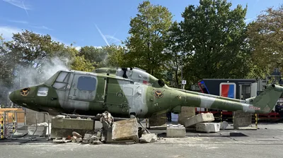 Soldat in taktischer Ausrüstung geht neben einem rauchenden Westland Lynx Hubschrauberwrack in der Training Base Weeze in Deckung