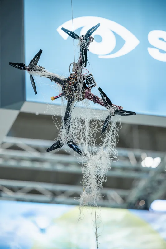 Quadrokopter-Drohne in einem Fangnetz als Exponat zur Drohnenabwehr auf einer Fachmesse ausgestellt