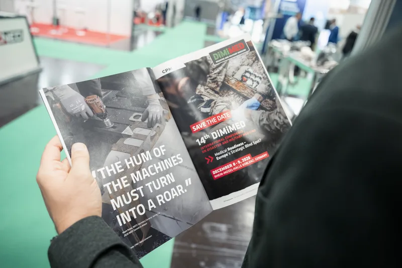 Besucher betrachtet auf einer Fachmesse eine Broschüre des CPM Verlags mit Ankündigung der DiMiMED-Konferenz und Zitat von Mark Rutte