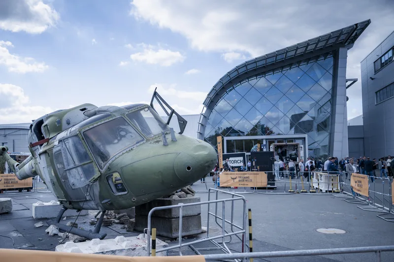Rumpfzelle eines Westland Lynx Hubschraubers auf Betonblöcken vor Werbebannern der Training Base Weeze auf einer Fachmesse