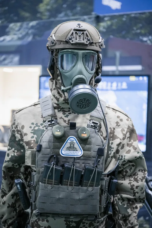 Militärische Schutzausrüstung mit Dräger-Atemschutzmaske und Tasmanian-Tiger-Plattenträger im Bundeswehr-Flecktarn auf einer Fachmesse